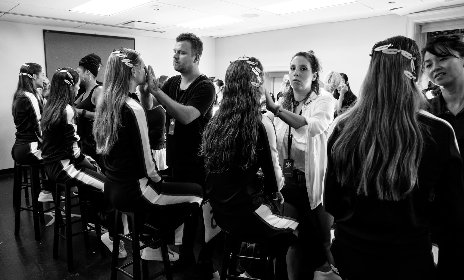 Row of models with sectioned, clipped long hair being prepared by stylists backstage