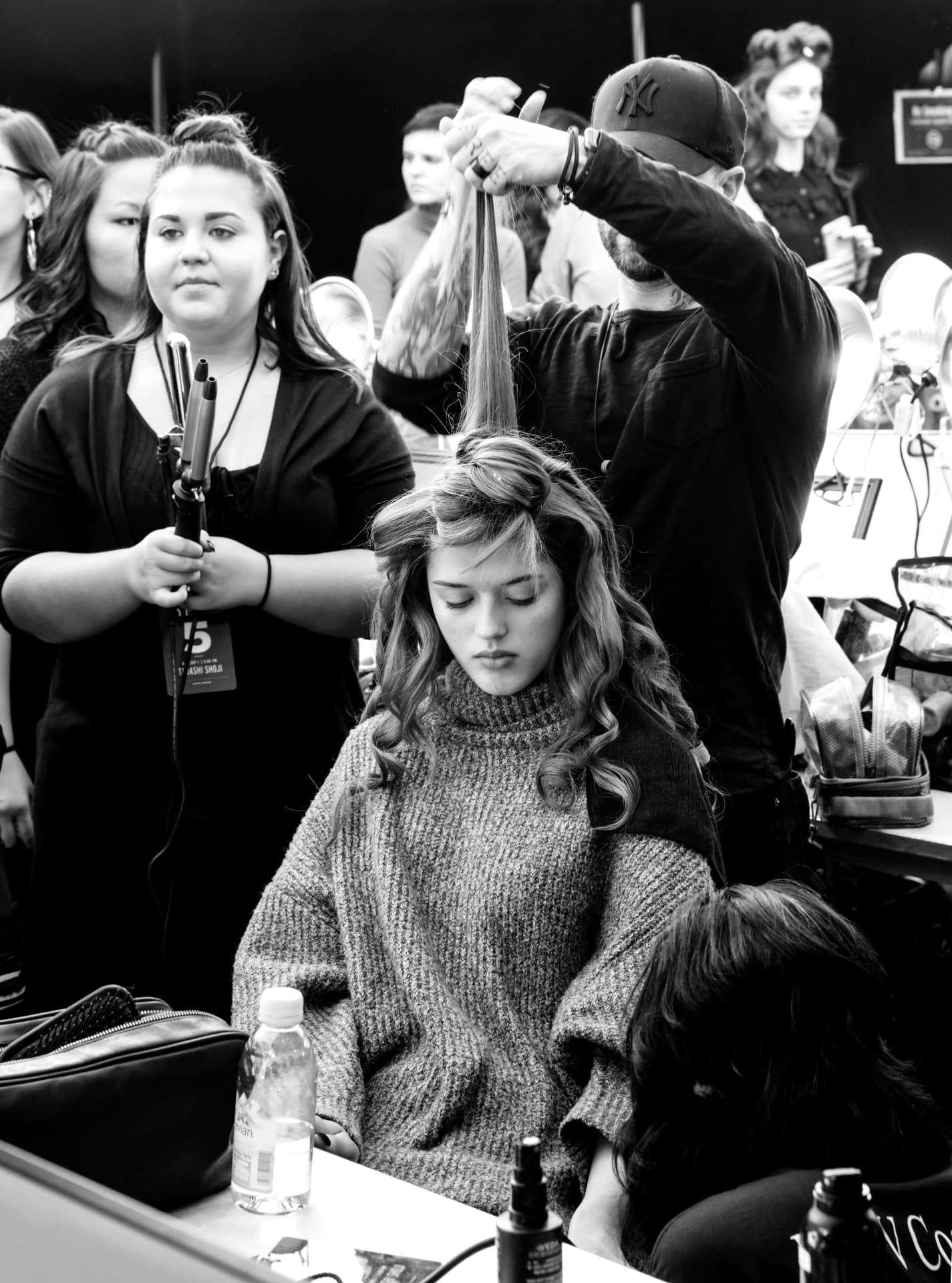 Stylist lifting a section of long blonde hair while the model waits in the chair
